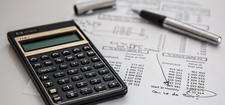 Zdjęcie przedstawia atrybuty księgowego: kalkulator, wykaz z rozliczeniem finansowym i długopis leżące na blacie biurka.